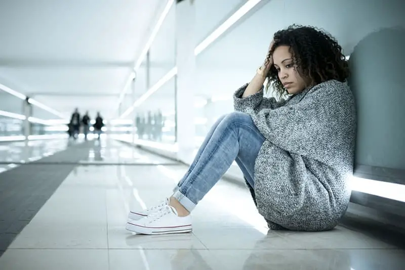 traurige Frau, die am Boden am Flughafen sitzt